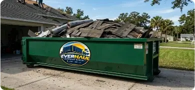 Green EverHaul roll-off dumpster full of torn-off roof shingles and underlayment outside a Lakeland, FL home