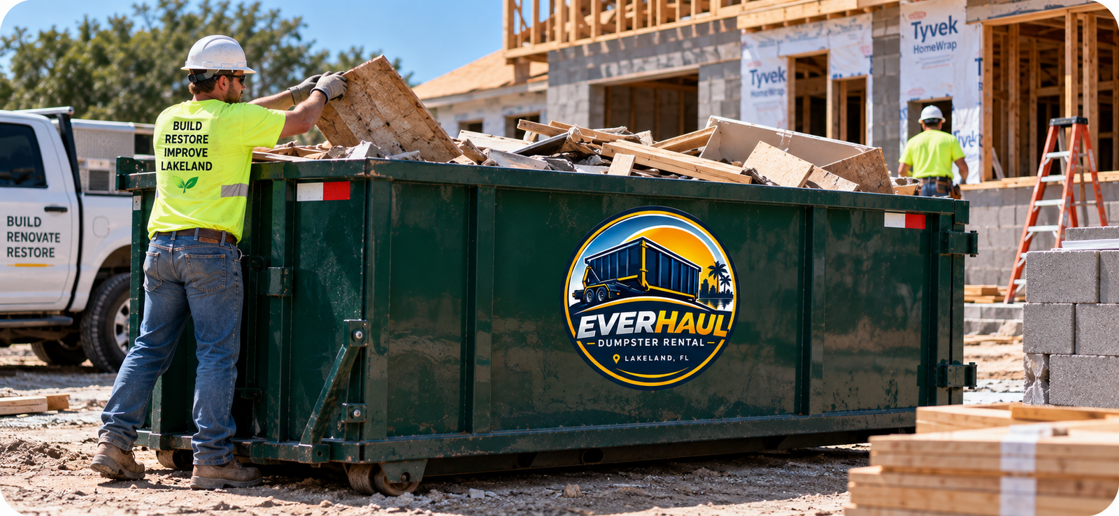 Construction worker loading wood framing and demolition debris into a green EverHaul roll-off dumpster at a Lakeland, FL new home construction site